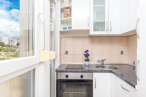 A compact kitchen with a built-in oven, a sink, and a window overlooking a cityscape. - Close to Znjan beach, spacious studio with balcony (Split)