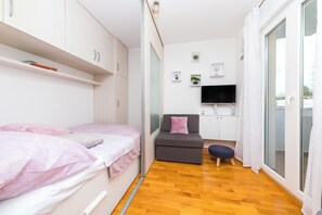 A compact bedroom with a bed, a small sofa, a TV, and a sliding glass door to a balcony. - Close to Znjan beach, spacious studio with balcony (Split)