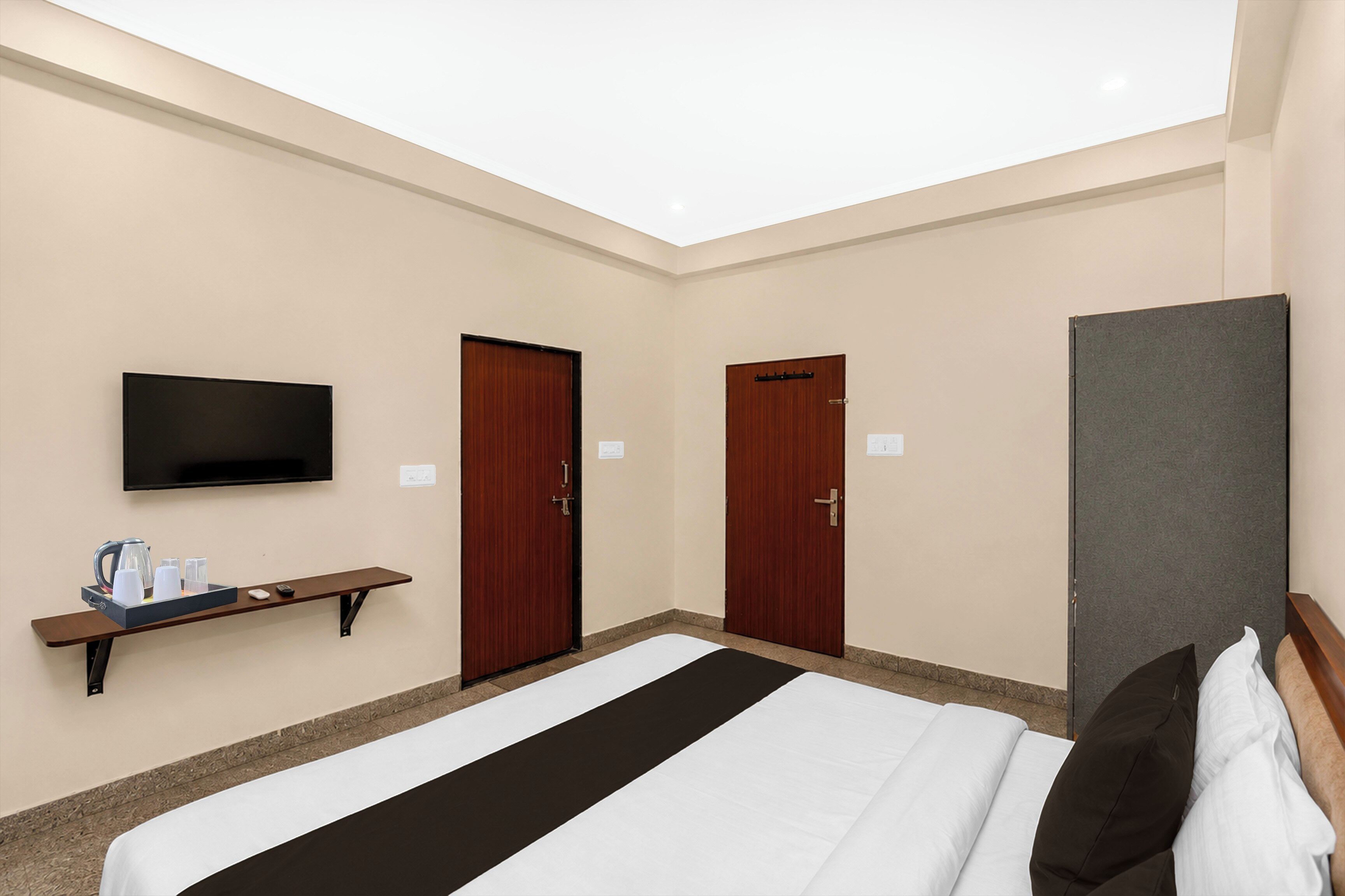 A hotel room with a bed, a television, a desk with a tray of amenities, and two doors.