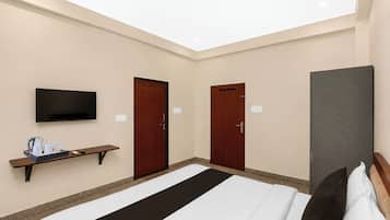 A hotel room with a bed, a television, a desk with a tray of amenities, and two doors.