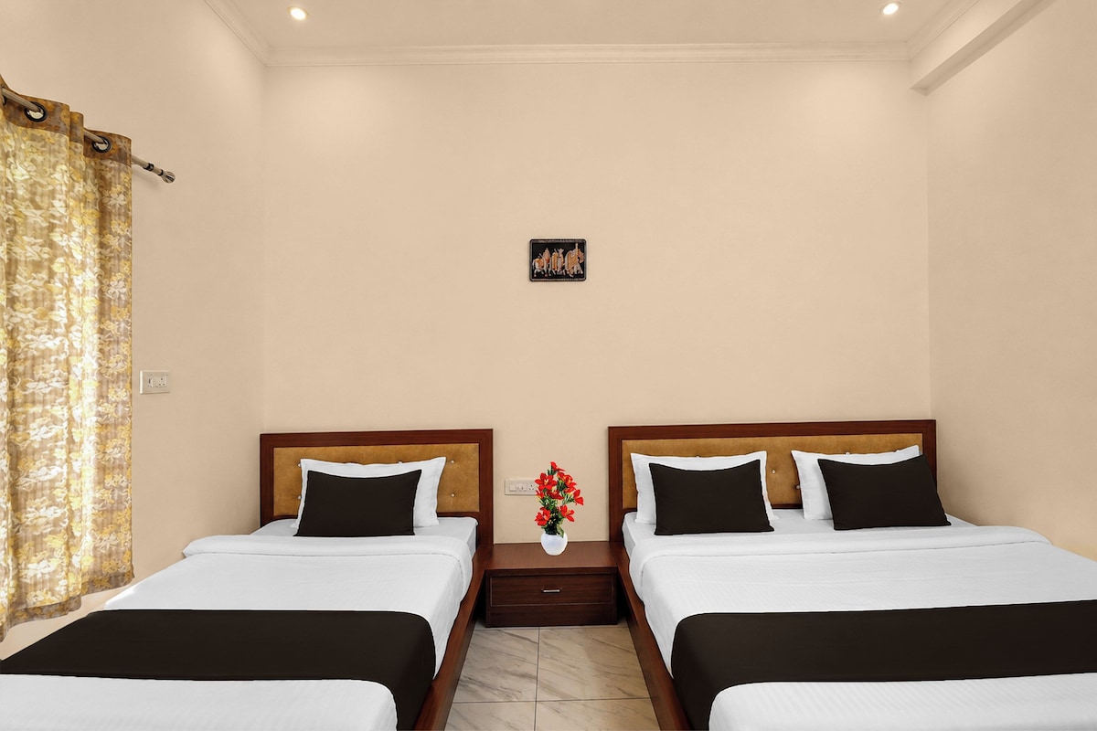 Una habitación de hotel con dos camas, una mesita de noche, un jarrón con flores y un cuadro colgado en la pared.