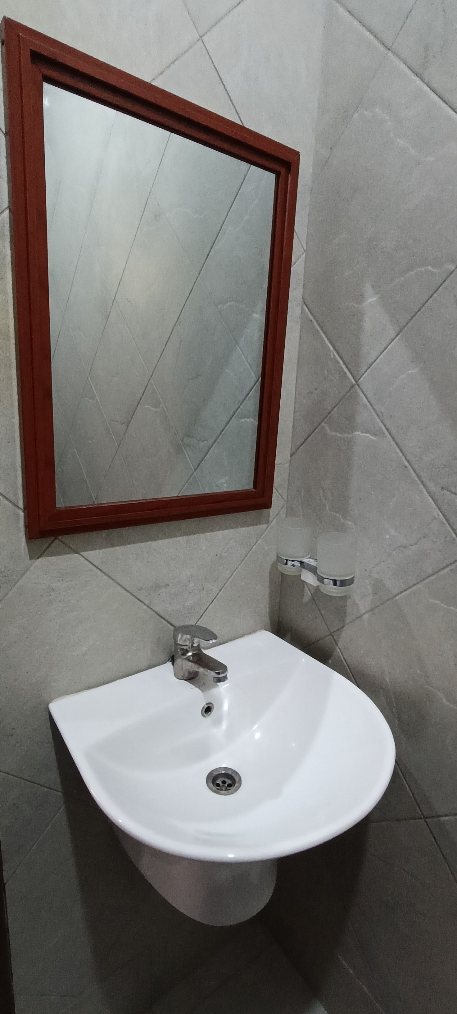 A bathroom with a white sink, a mirror with a wooden frame, and tiled walls.
