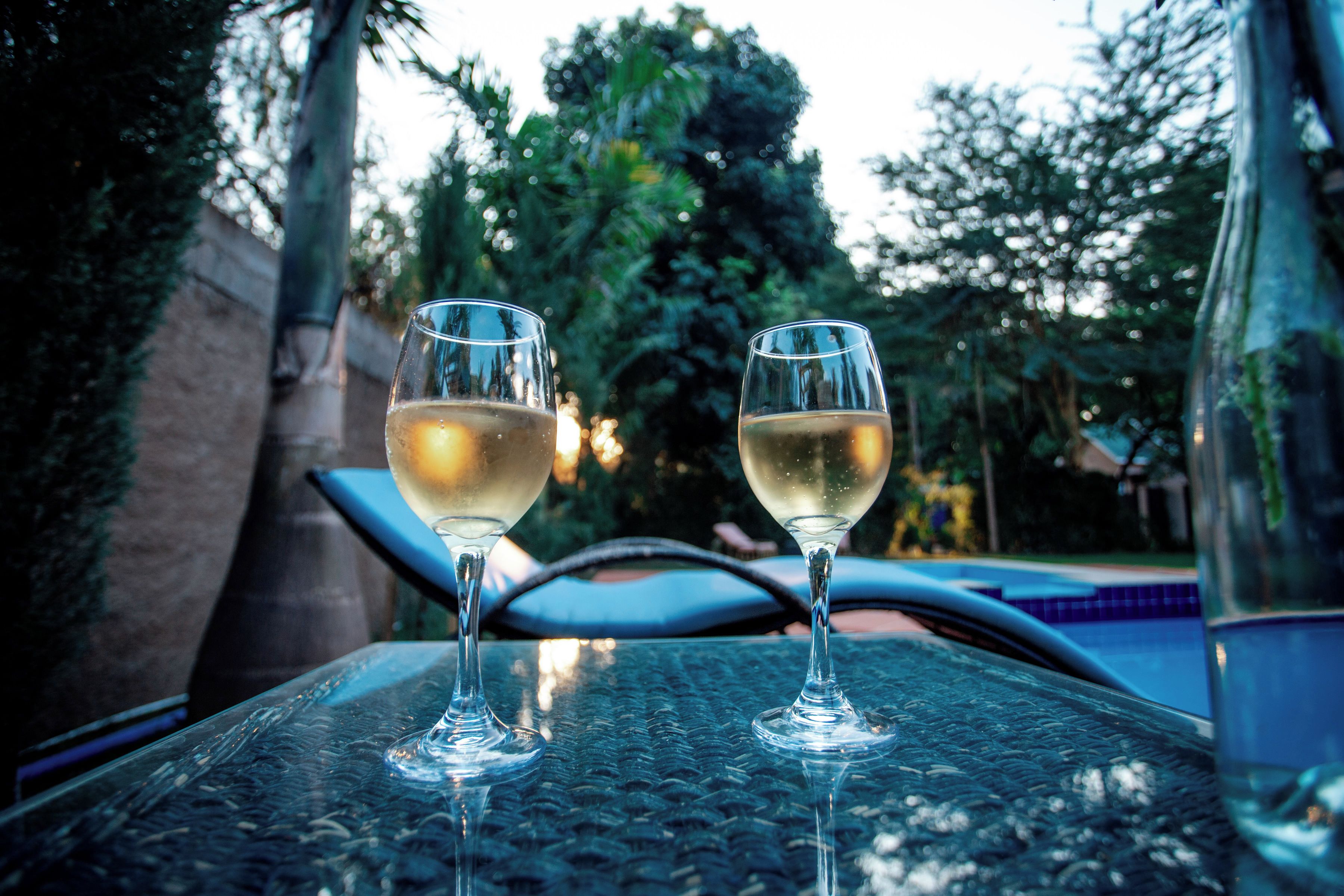 Two glasses of white wine on a glass table with a pool in the background.