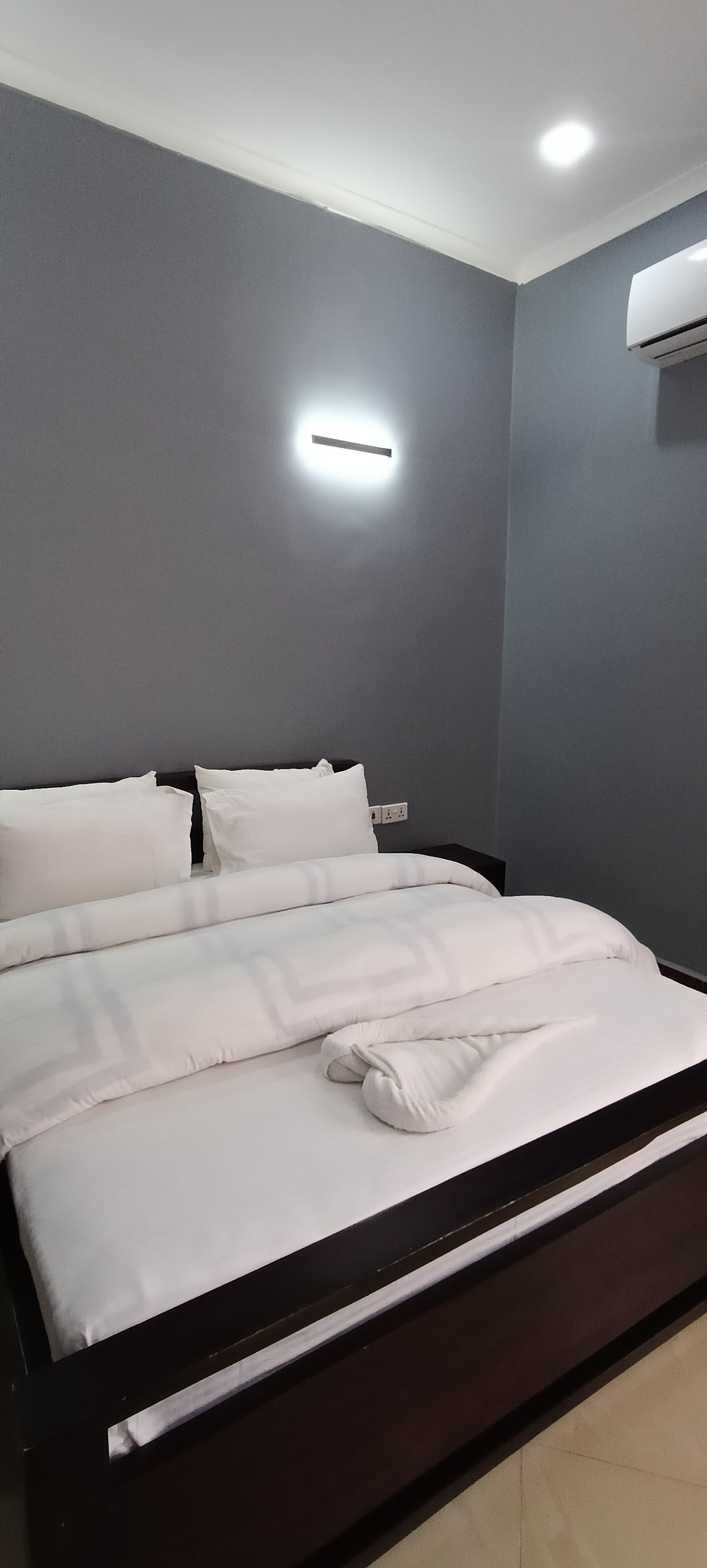 Un dormitorio moderno con una cama grande, paredes grises y una lámpara en el techo.