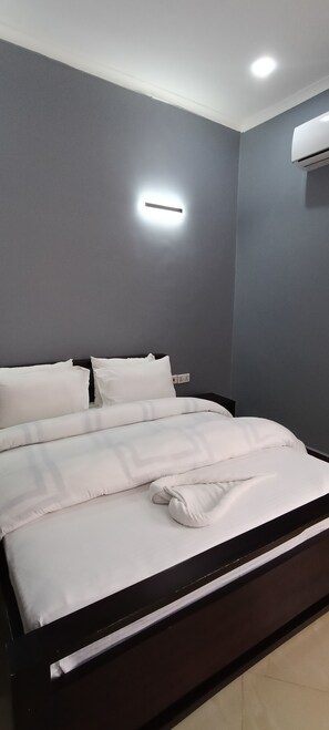 A modern bedroom with a large bed, grey walls, and a ceiling light. - Tranquil 2-bedroom apartment with AC in Moshi (Kilimanjaro Region)