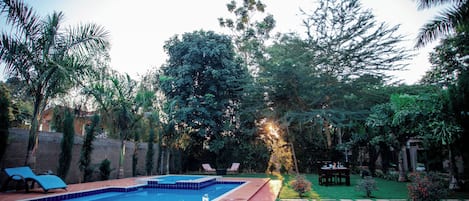A swimming pool with a tiled deck, surrounded by a garden with various plants and trees.