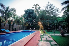 Una piscina amb un terra solcat, envoltada d'un jardí amb diverses plantes i arbres.