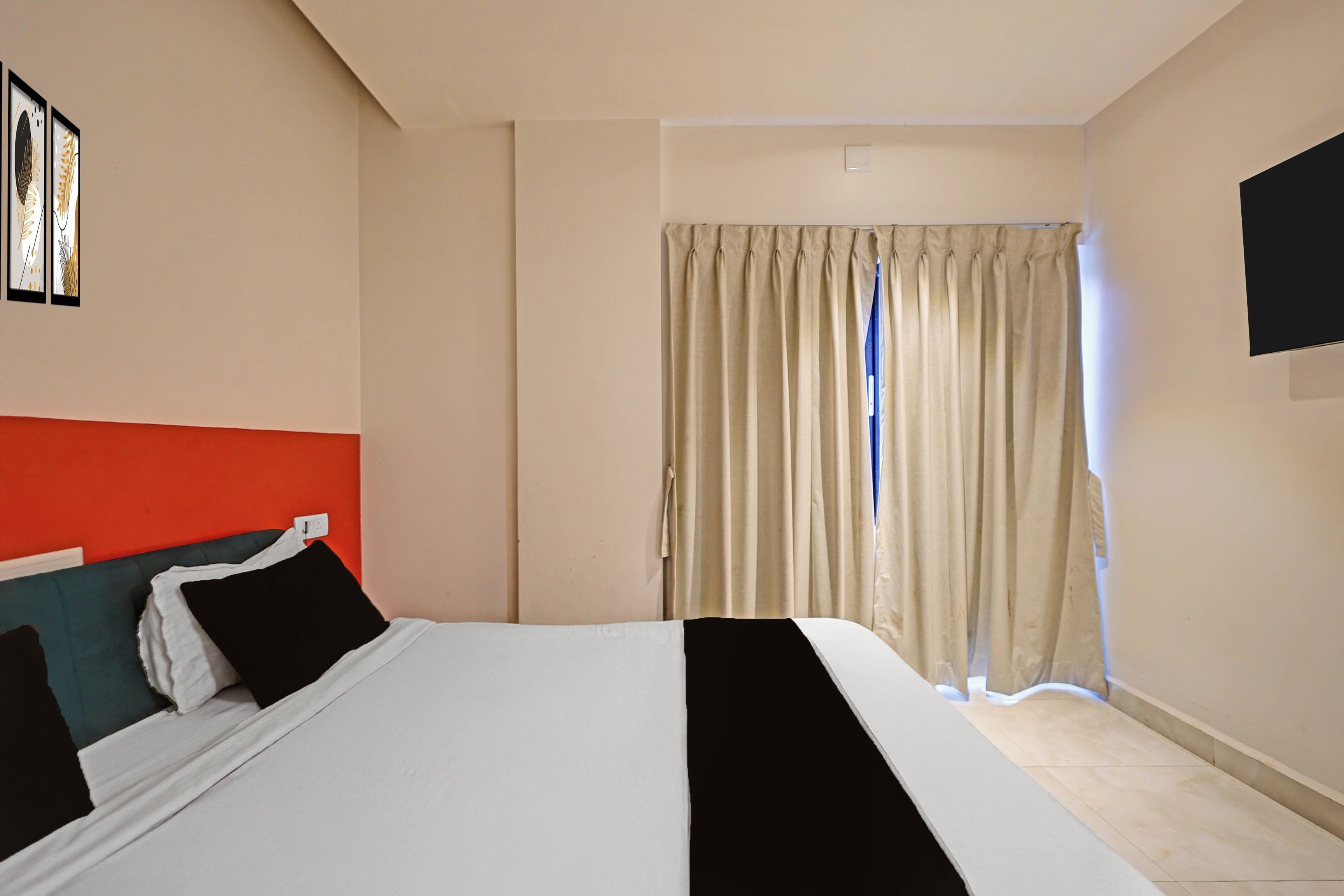A hotel room with a bed, a flat-screen TV, and a window with curtains.
