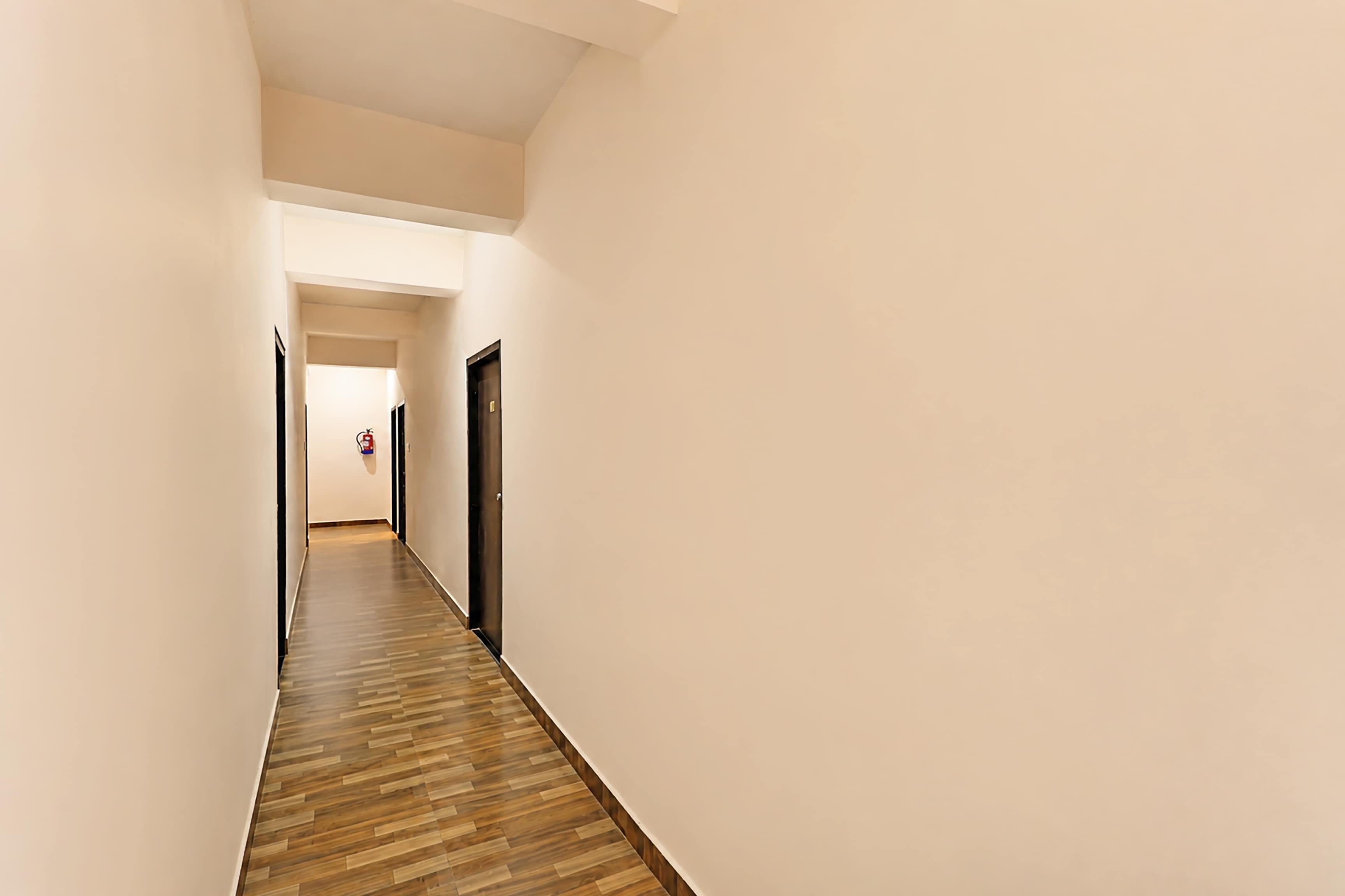 Un pasillo estrecho con piso de madera y paredes blancas, que conduce a una puerta al final.