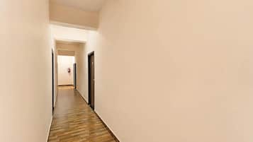 Un pasillo estrecho con piso de madera y paredes blancas, que conduce a una puerta al final.