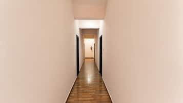 A narrow, well-lit hallway with wooden flooring and plain walls, leading to a door at the end.