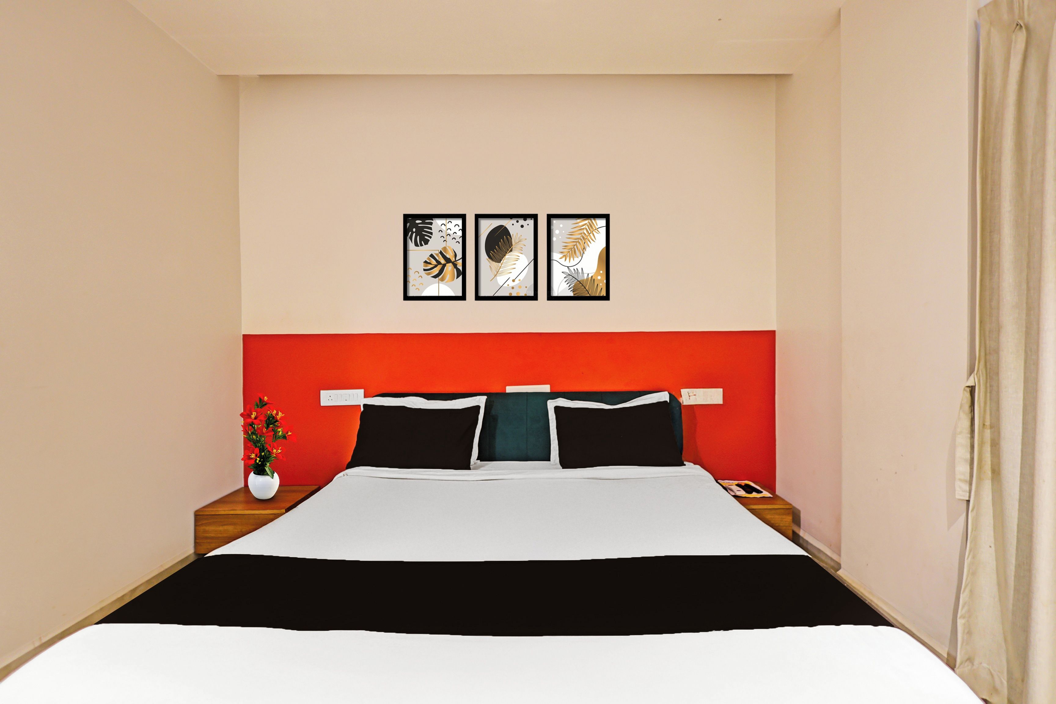 Habitación de hotel con cama, mesita de noche, florero con flores y tres cuadros en la pared.