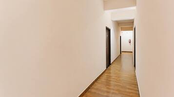 A corridor with wooden flooring and plain walls, leading to a door at the end.