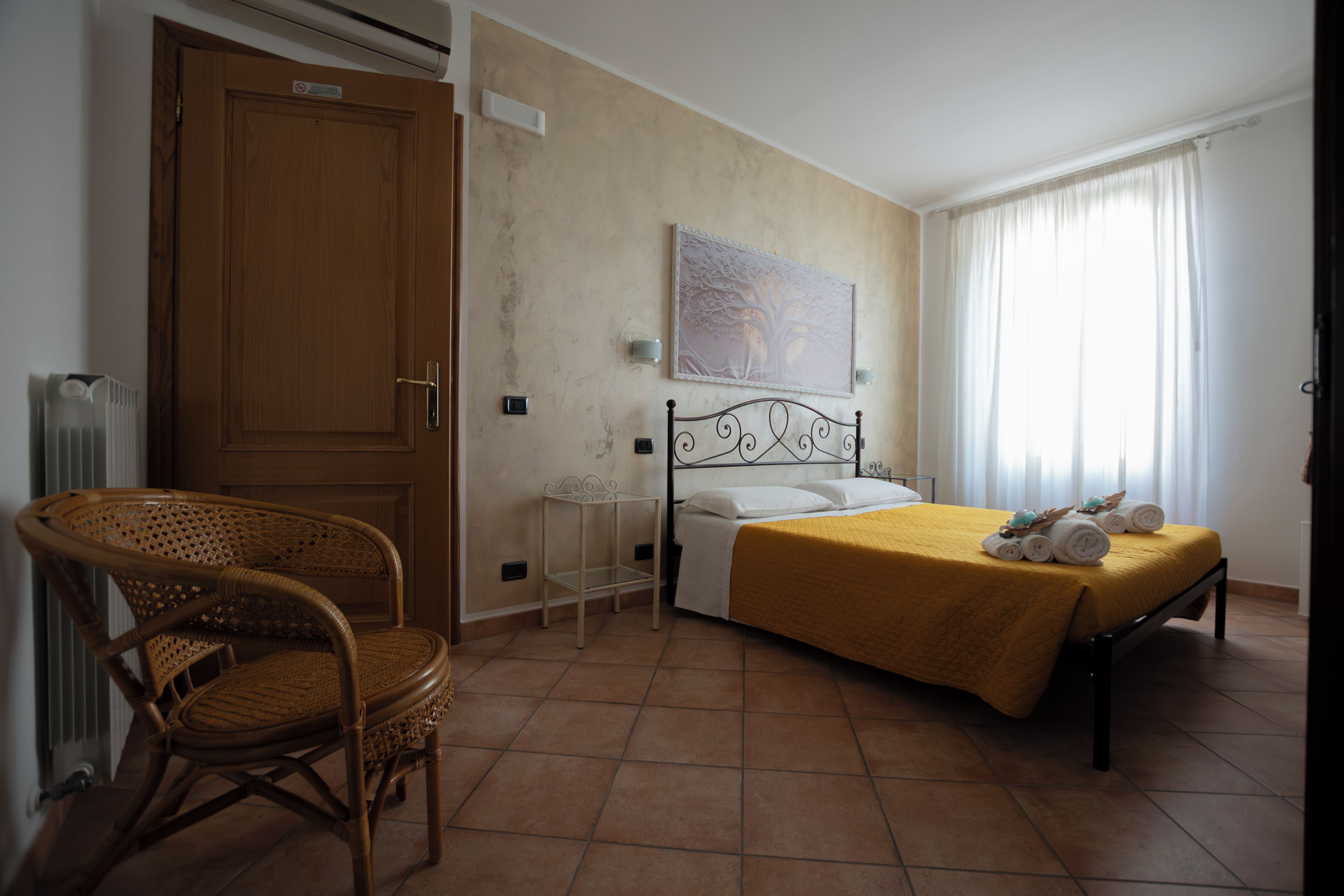 Un dormitorio con cama, una silla, un radiador, una lámpara de pared y una ventana con cortinas.