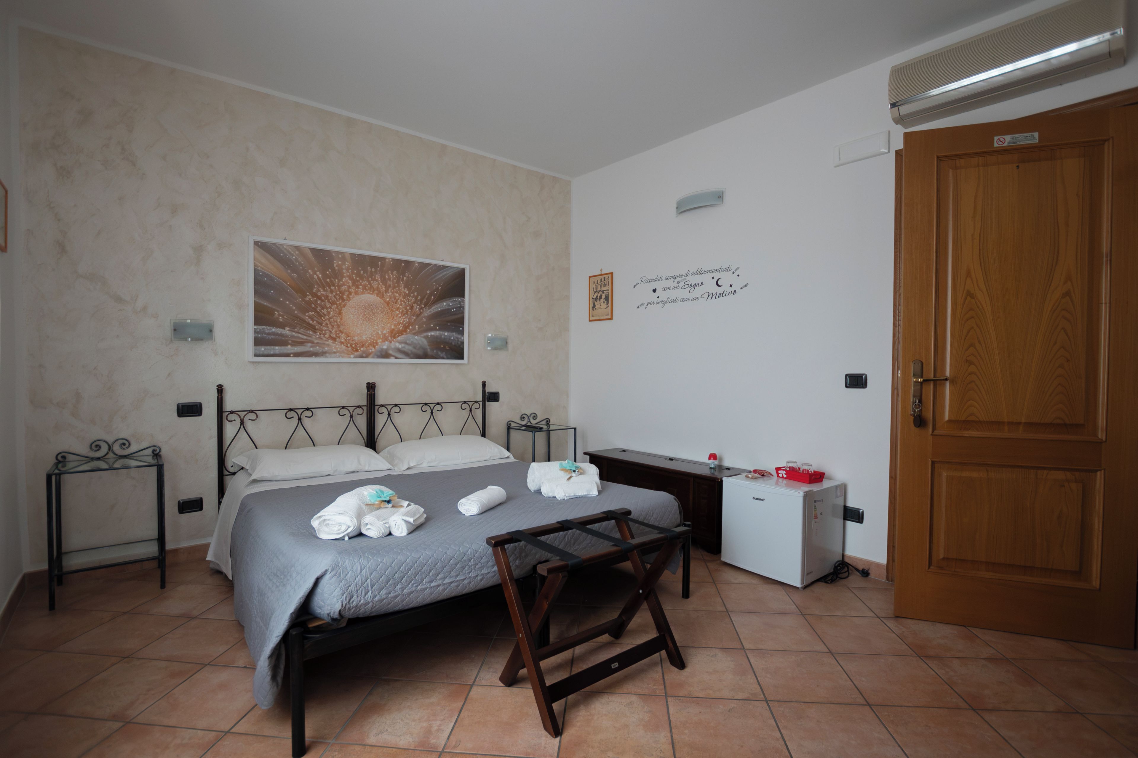 Un dormitorio con una cama, un escritorio, una silla, un radiador, una puerta y una obra de arte colgada en la pared.