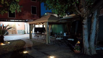 Un patio al aire libre con mesas y sillas, un área de estar cubierta y un edificio en el fondo.