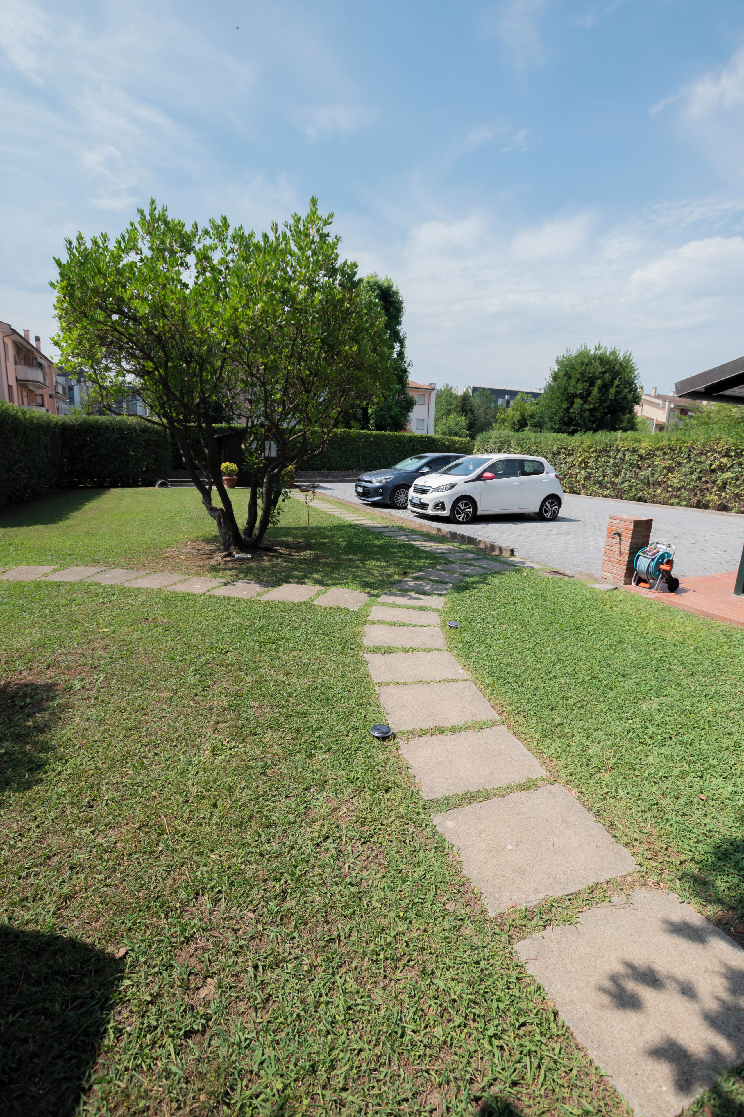 A residential area with a paved pathway leading to a driveway where cars are parked.