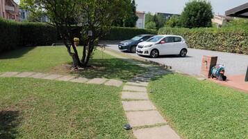 A residential area with a paved pathway leading to a driveway where cars are parked.