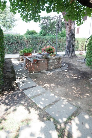 Un jardín con una jardinera de piedra, plantas en macetas y un árbol.