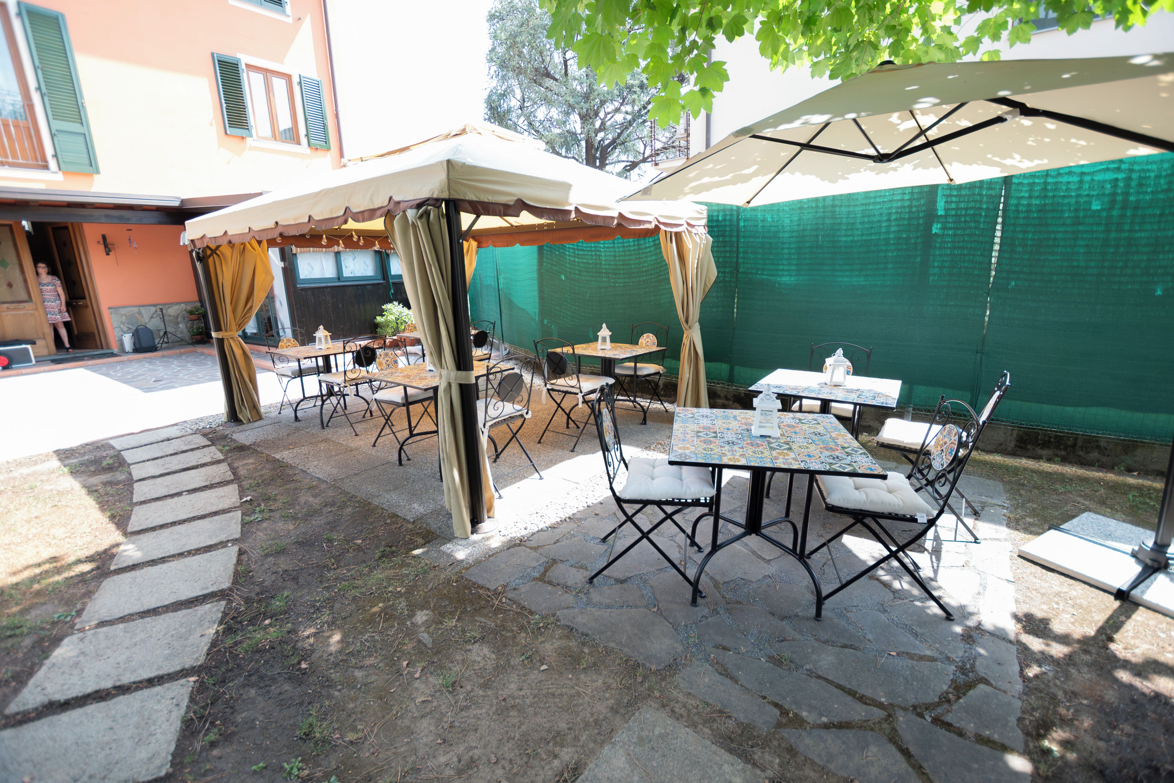 Un patio al aire libre con mesas y sillas, un espacio de estar techado y un sendero de piedra.