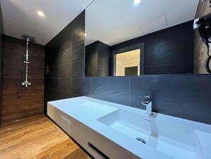 A modern bathroom with a large white sink, dark tiled walls, and a wooden floor. - Villa Albero (Torremolinos)