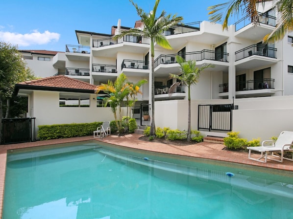 A modern residential building with a swimming pool, balconies, and tropical landscaping. - Windsurfer Resort (Gold Coast)