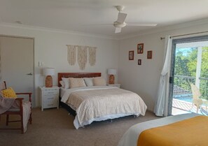 Ein Schlafzimmer mit Bett, Nachttischen, einem Sessel, einem Balkon mit Blick und einem Deckenventilator.