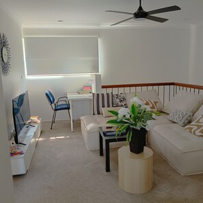 Ein Wohnzimmer mit Sofa, Couchtisch, Fernseher, Sessel und Deckenventilator.