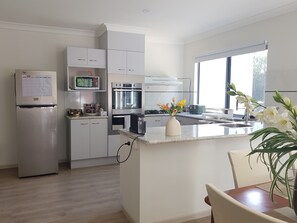 Eine moderne Küche mit weißen Schränken, einem eingebauten Ofen, einer Mikrowelle und einem Kühlschrank. Ein Fenster sorgt für natürliches Licht und eine kleine Kücheninsel ziert sich mit einer Blumenvase.