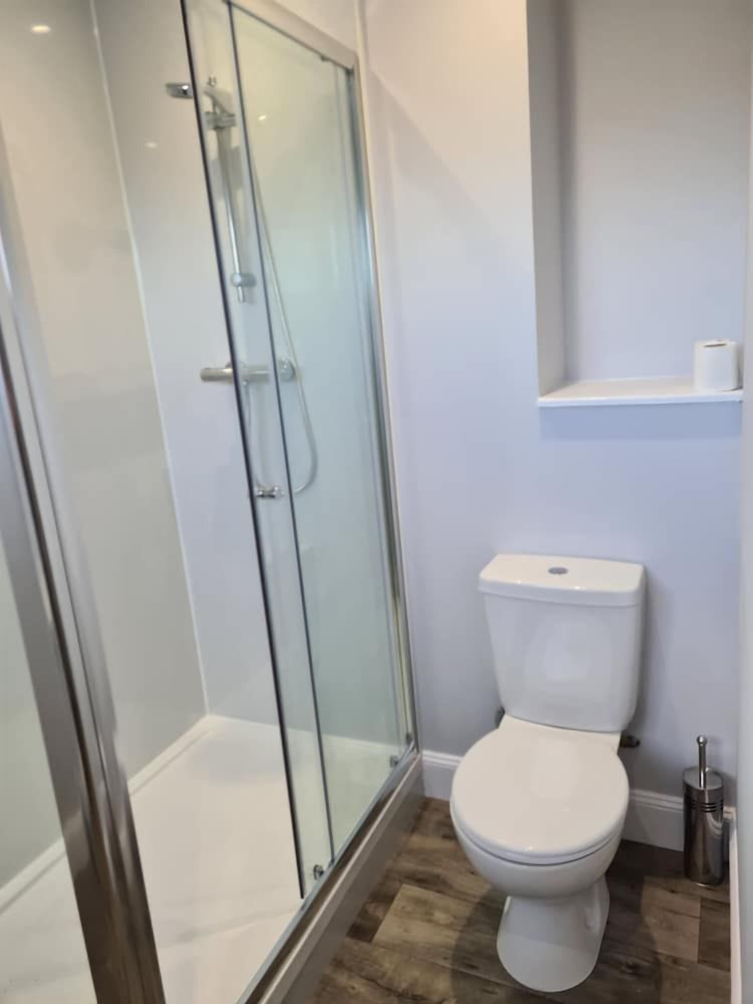 Ein modernes Badezimmer mit einer gläsernen Dusche, einer weißen Toilette und einem Metall-Mülleimer.