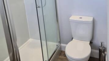 Ein modernes Badezimmer mit einer gläsernen Dusche, einer weißen Toilette und einem Metall-Mülleimer.