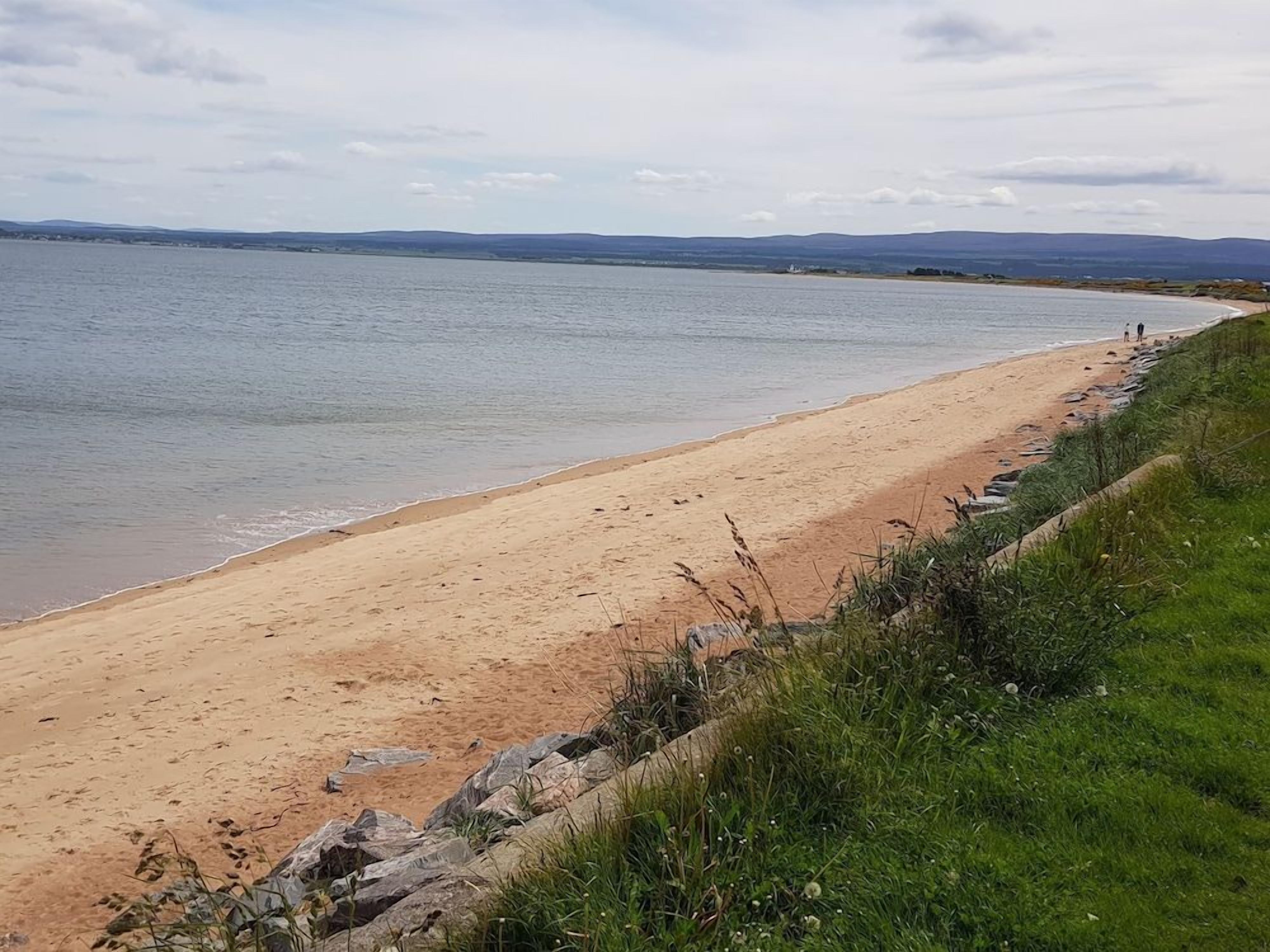 Ein Strand mit freiem Blick auf das Wasser und sanfte Hügel in der Ferne.