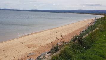Ein Strand mit freiem Blick auf das Wasser und sanfte Hügel in der Ferne.