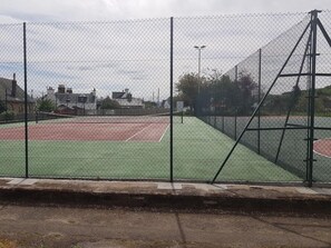 Pista de tenis cercada por una malla metálica y una red.