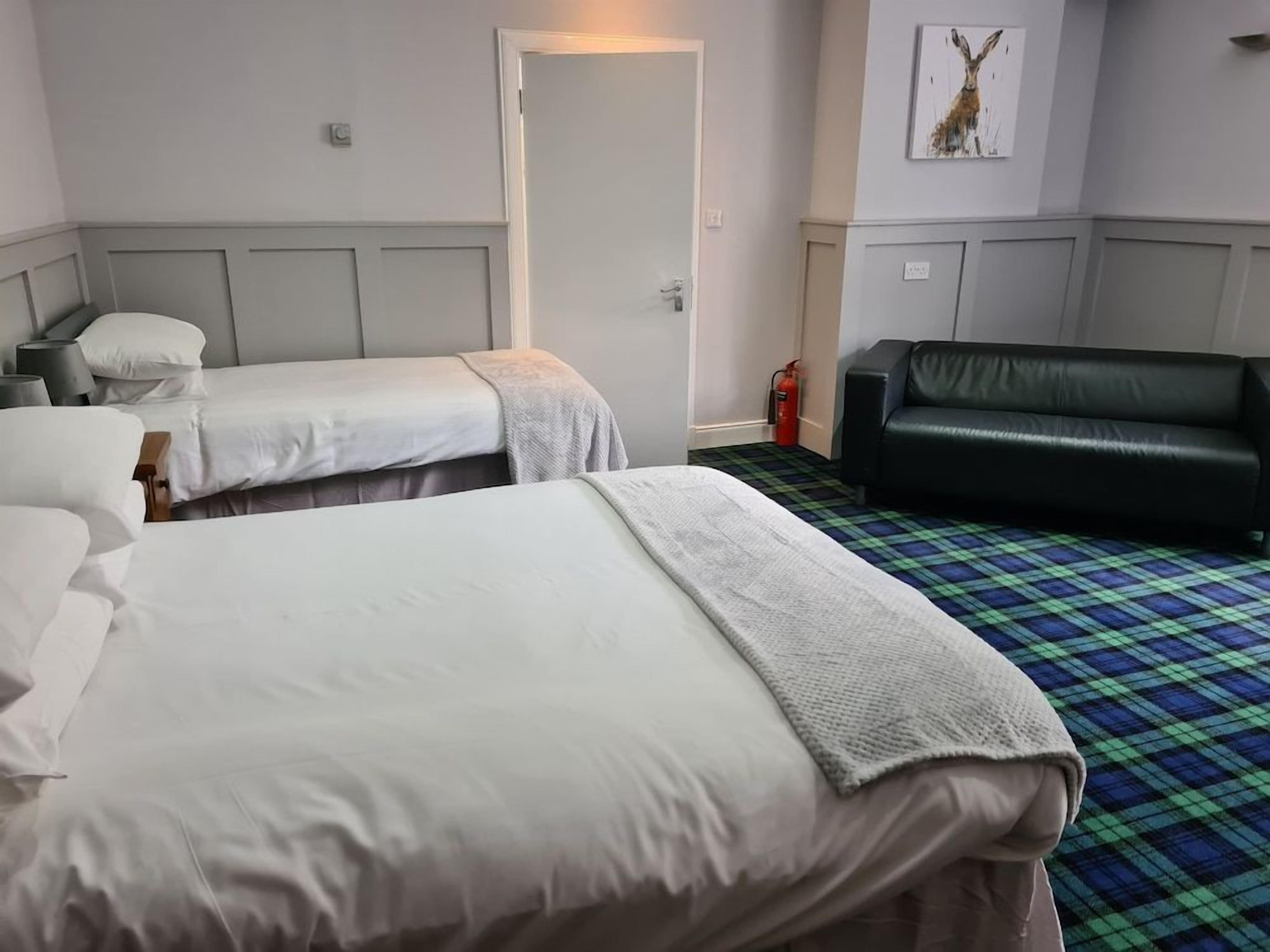 Ein Hotelzimmer mit zwei Betten, einer Couch, einem Feuerlöscher und einer Tür.