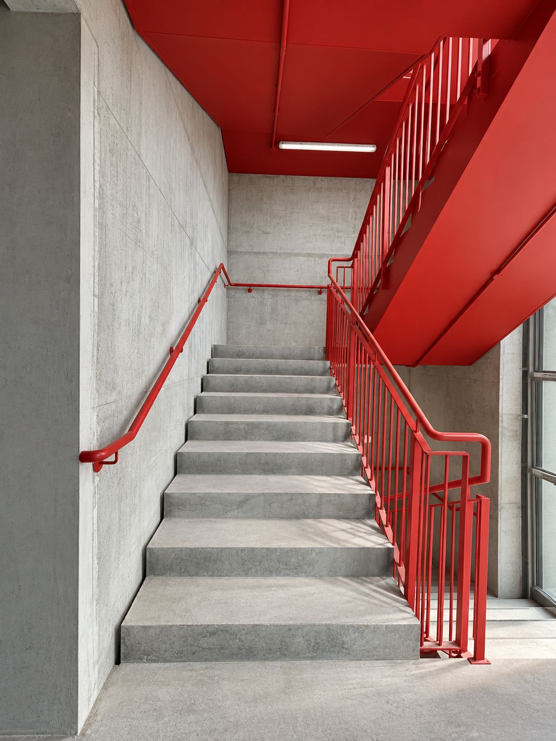 Una escalera con barandas rojas y piso de concreto.