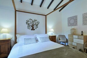 Quarto com cama, duas luminárias laterais, uma cadeira, cômoda e decoração nas paredes.