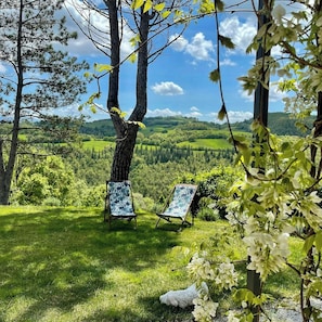 An outdoor seating area with two chairs and a table, surrounded by trees and a view of a green landscape. - Cottage surrounded by a romantic garden (Gubbio)