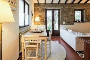 A cozy room with a stone wall, a wooden table with chairs, a sofa, and a lamp. - Cottage surrounded by a romantic garden (Gubbio)