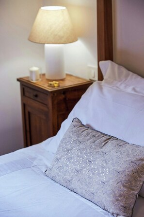 A neatly made bed with white linens and a decorative pillow, a bedside table with a lamp, and a wooden nightstand. - Cottage surrounded by a romantic garden (Gubbio)