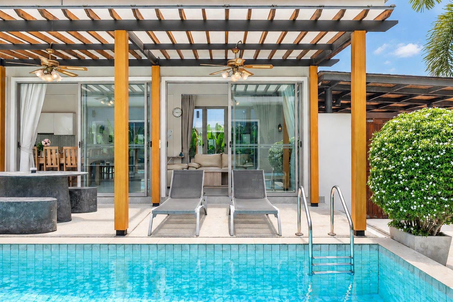 A poolside area with lounge chairs, a covered seating area, and a view of the interior through glass doors.