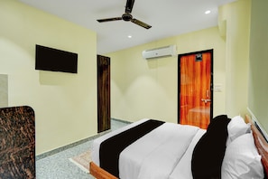 A hotel room with a bed, a ceiling fan, a mounted TV, an air conditioning unit, and a wooden door. - Palette Mansarover Extension (Jaipur)