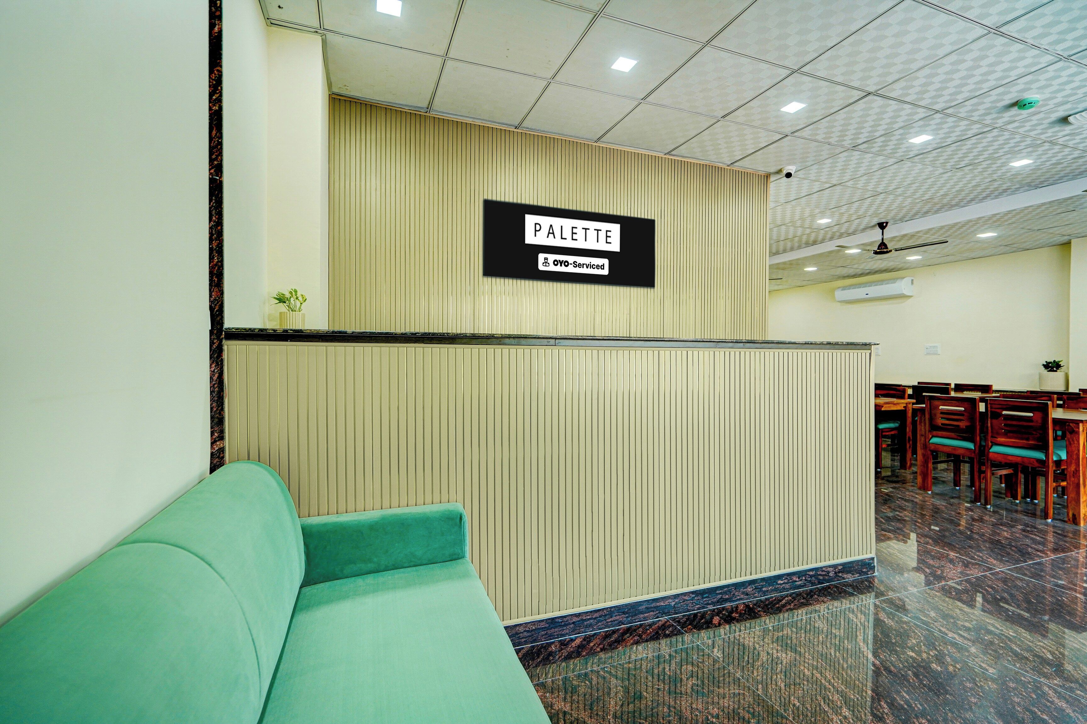 A reception area with a sign that reads 'PALETTE' and 'OYO-Serviced.' There is a green sofa and a wooden reception desk.