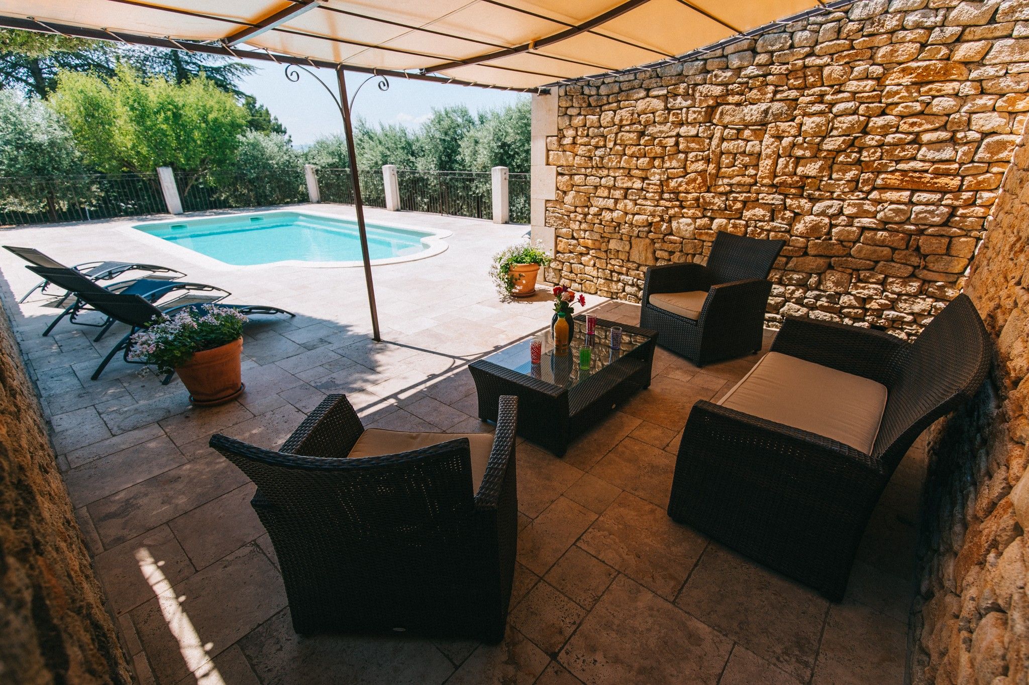 Un espace extérieur aménagé en terrasse, avec un mur en pierre, une piscine et du mobilier de jardin.