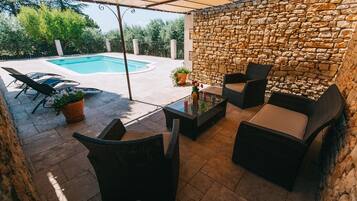 Un espace extérieur aménagé en terrasse, avec un mur en pierre, une piscine et du mobilier de jardin.