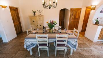 A dining area with a table set for two, wooden chairs, a chandelier, and a vase with flowers.