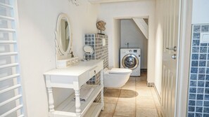 Casa de banho pequena com toucador branco, sanita, máquina de lavar e espelho.