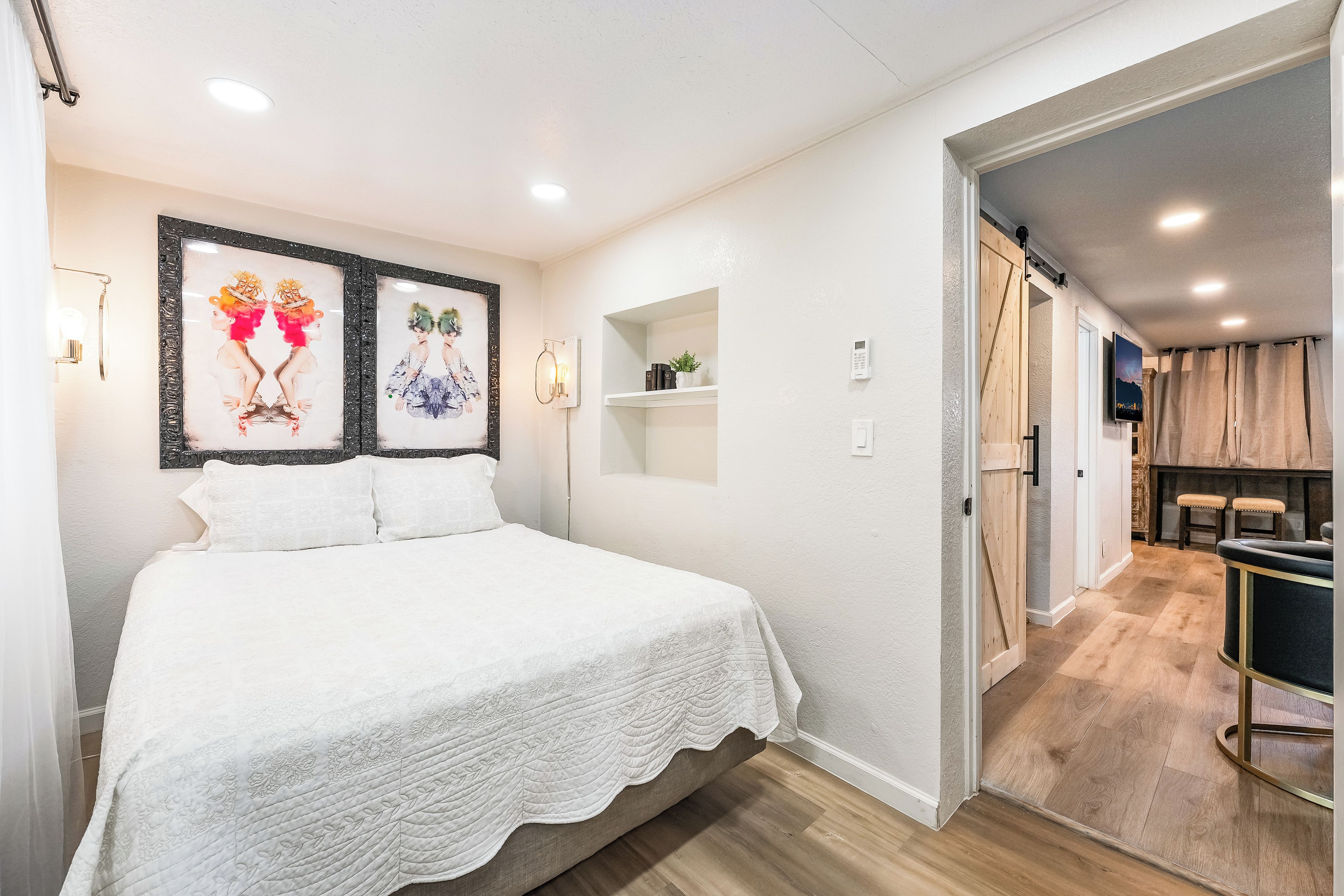 Een slaapkamer met een bed, een wandplank met boeken en een deur naar een gang.