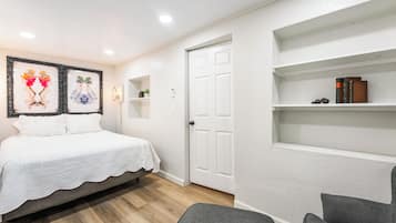 A bedroom with a bed, a door, a shelf with books, and a framed artwork on the wall.