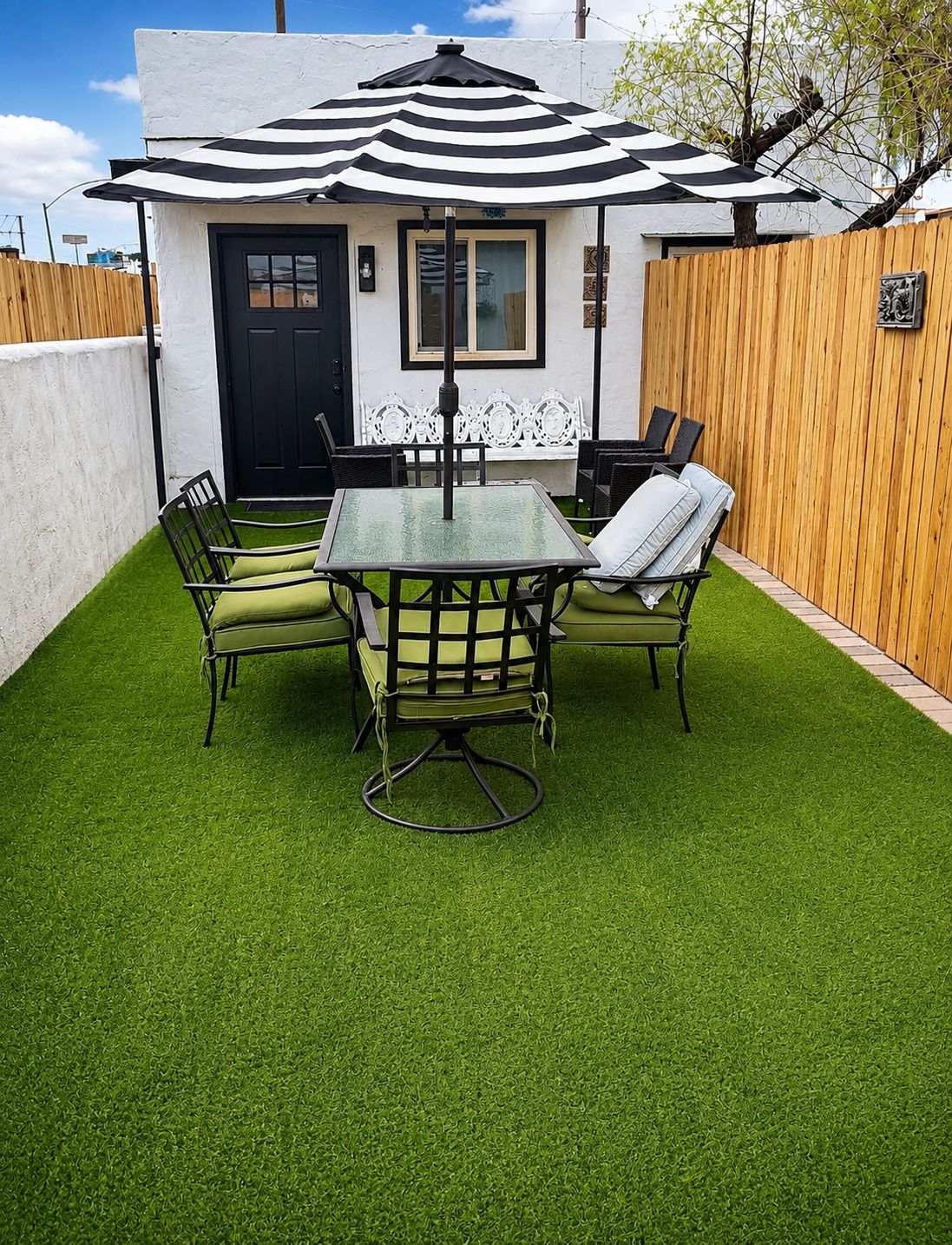 A patio with a glass table and chairs, a black and white striped umbrella, and a wooden fence.